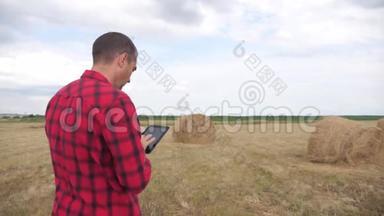 智慧农业理念.. 一个农夫在一个数字生活平板电脑上的田野里研究干草堆。 慢动作
